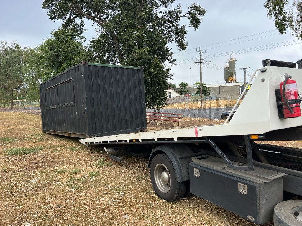Modified shipping container with serving hatch being unloaded by tilt tray at Maddingley