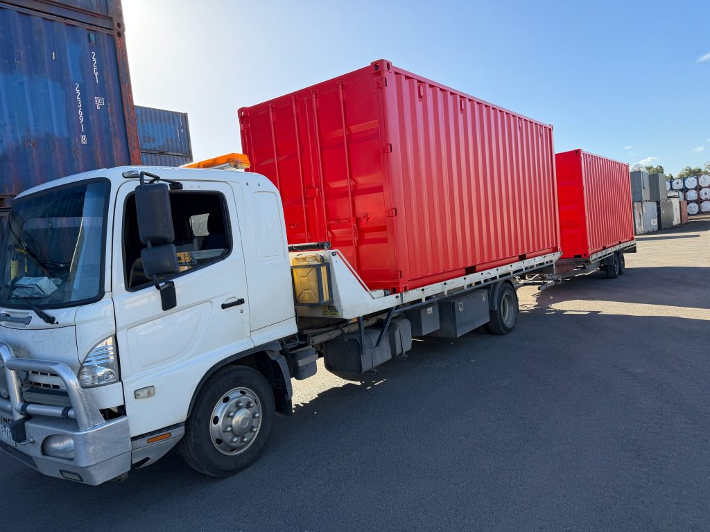 Two red shipping containers loaded on a tilt tray and trailer at the Tottenham yard